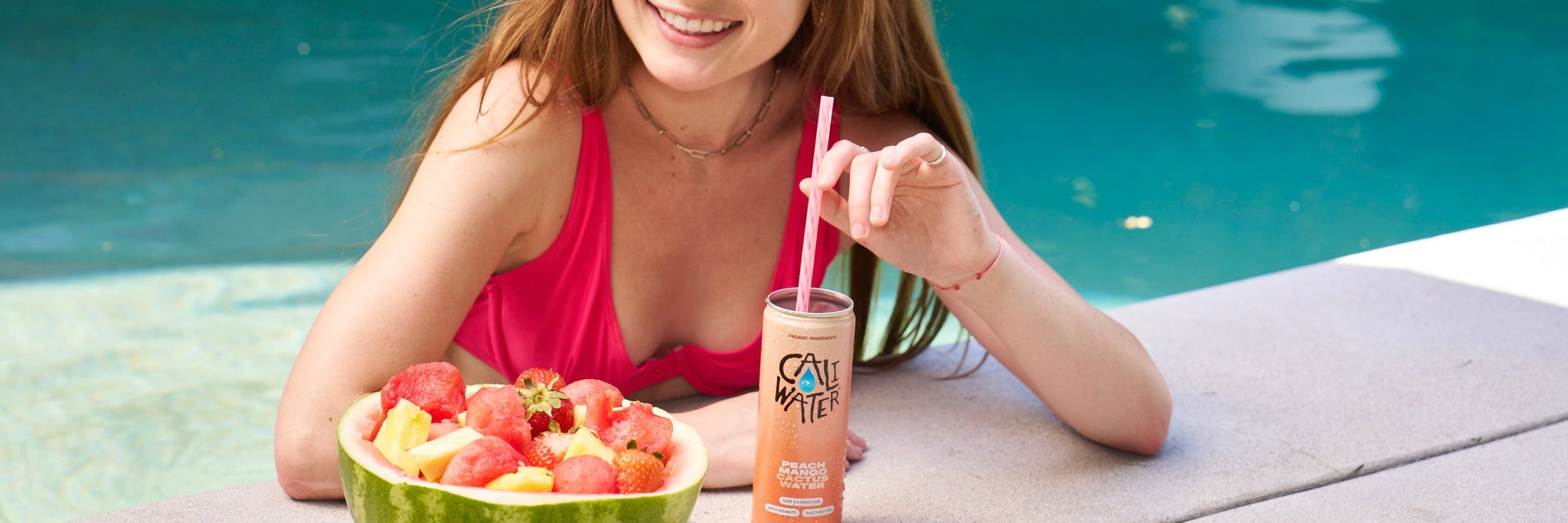Woman sipping Caliwater by the pool with fruit 