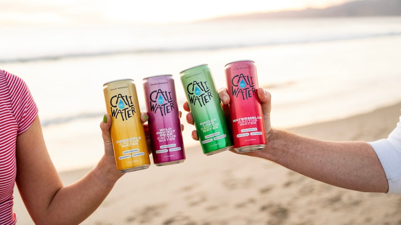 Two people holding Caliwater Cactus Water at the beach